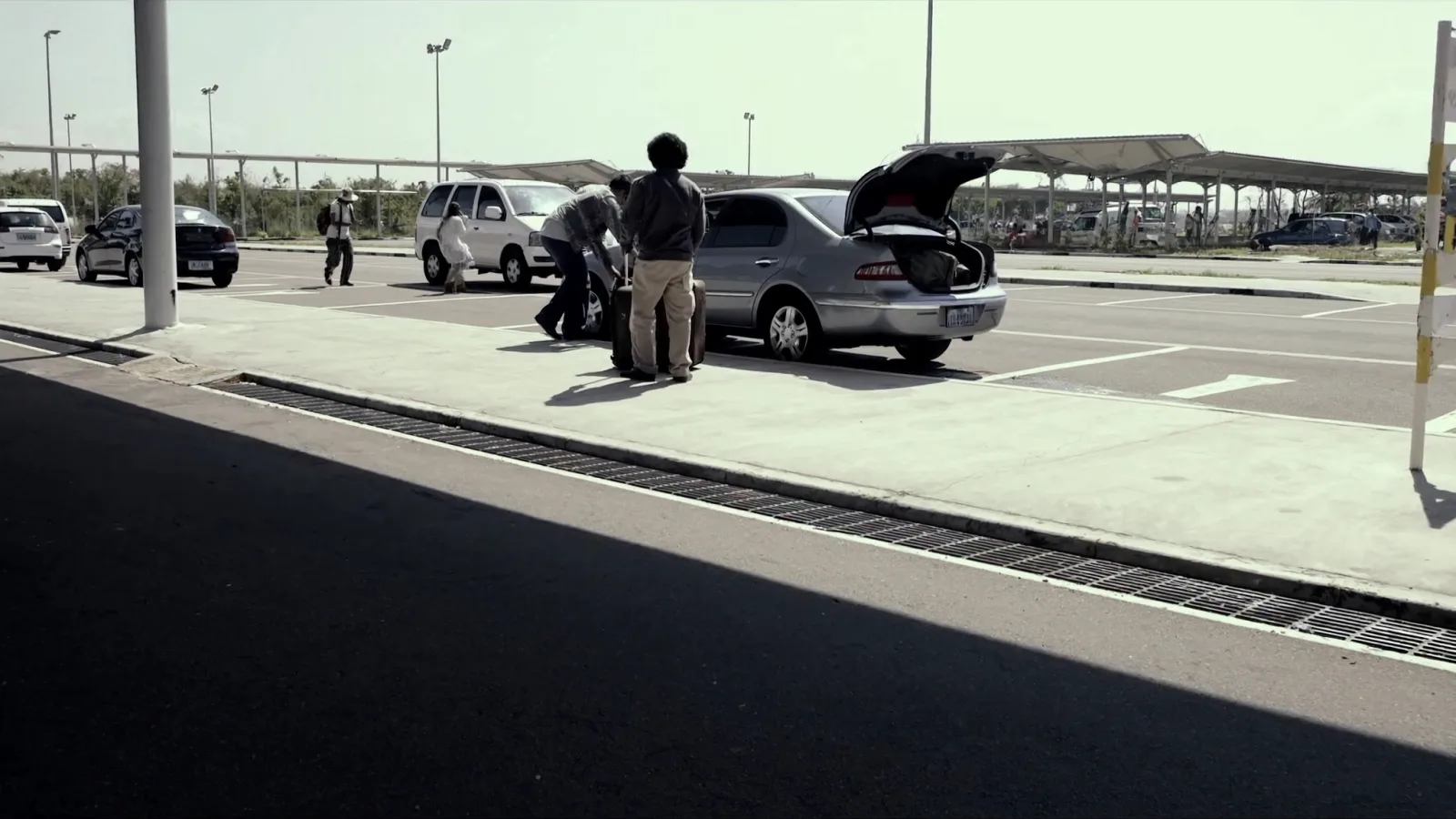 Carro parado no meio-fio de desembarque do terminal, com passageiro retirando mala do porta-malas