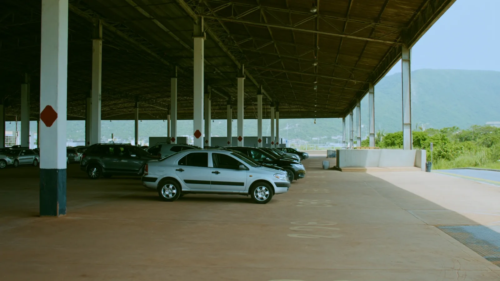 Fileira de vagas cobertas num estacionamento perto do aeroporto de Confins, sob galpão metálico