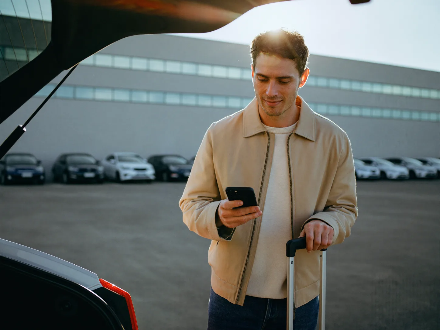 Viajante conferindo a reserva no celular ao lado do carro, no estacionamento do aeroporto